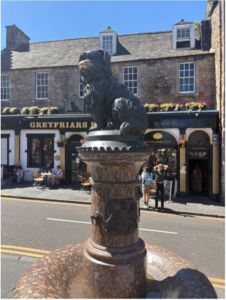 The Greyfriars Bobby statue, a bronze terrier atop a granite fountain, stands in front of the historic Greyfriars pub in Edinburgh.