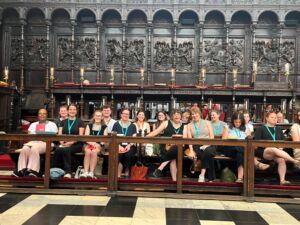 NAFAns wearing teal lanyards sit in the historic choir stalls of King’s College Chapel before Evensong. Ornate paneling, candleholders, and Gothic architectural details form the backdrop.