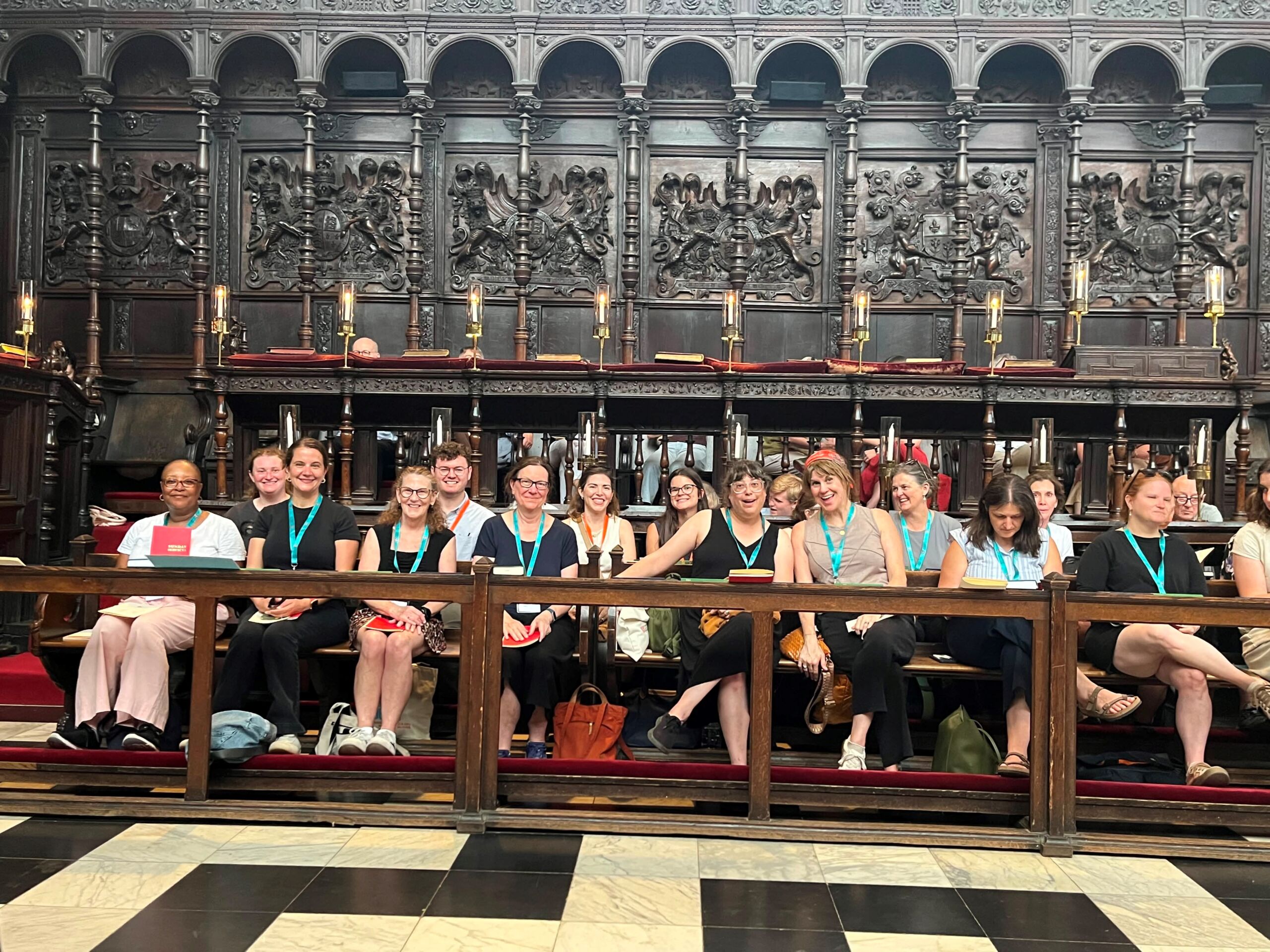 NAFAns wearing teal lanyards sit in the historic choir stalls of King’s College Chapel before Evensong. Ornate paneling, candleholders, and Gothic architectural details form the backdrop.