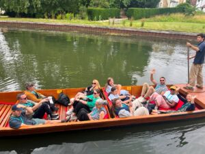 A group of NAFAns relax in a wooden punt on the River Cam while a punter stands at the stern using a long pole to guide the boat.