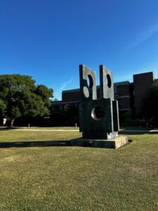 Abstract outdoor sculpture at Churchill College featuring large metal panels with circular cutouts.
