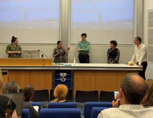Five people stand in front of a lecture hall behind a long desk, participating in a panel at St Andrews.